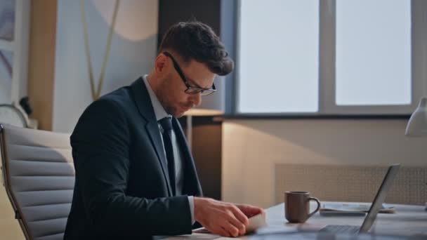 家のオフィスの閉鎖に座っているラップトップのキーボードをタイプする男の作家 仕事のために現代コンピュータを使用して眼鏡の真剣なスマートな作家 中年男性は屋内で新しいアイデアを作成するノートを書いています — ストック動画