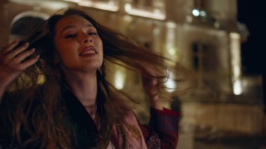 Şen şakrak dans eden kadın şehir sokağında yalnız poz veriyor. Mutlu gülümseyen kız geceleri zarif bir binanın önünde vücudu hareket ettiriyor. Boş kasaba bölgesinde son moda, tasasız dansçı..