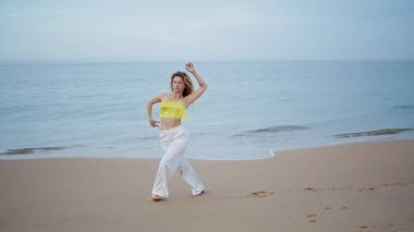 Güzel plajda çağdaş stilde pratik yapan bir kız. Zarif, genç, sarışın, hareketli, şehvetli bir kamera. Genç kıvırcık kadın ıslak kumlu deniz kıyısında yaz akşamı dans ediyor. Modern koreografi.