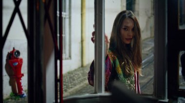 Vitrinden şık kıyafet manzaralı akşam poz verdirme caddesi. Cam kapılı şehir binasının yanında duran tasasız stil sahibi kadın. Kameraya bakan güzel genç kız hafta sonunu yalnız geçiriyor..