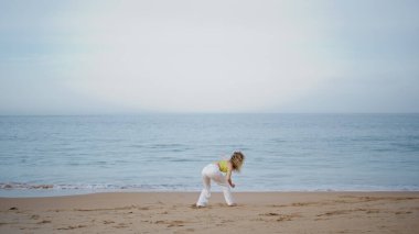 Sahilde sahne alan enerjik dansçı akşam okyanus esintisinin tadını çıkarıyor. Kum Denizi Sahili 'nde çağdaş dans eden yetenekli genç bir kadın. Vücudunu hareket ettiren esnek kız duygularını dışa vuruyor..