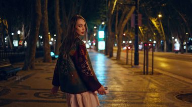 Arka planda yürüyen kız gece geç saatlerde kameraya dönüyor. Kendine güveni tam genç bir kadın, gece kaldırımlarına çıkıyor, sokak lambaları yanıyor. Muhteşem, rahat bir model. Şehir merkezinde geziniyor.