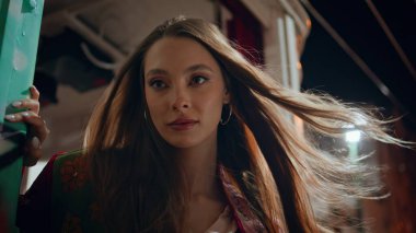 Alacakaranlık akşamında poz veren modaya uygun bir model. Rüzgâr tarafından savrulan uzun saçlı güzel bir genç kadının portresi. Muhteşem kendine güvenen kız yaz gecesi şehir binasında dikiliyor..