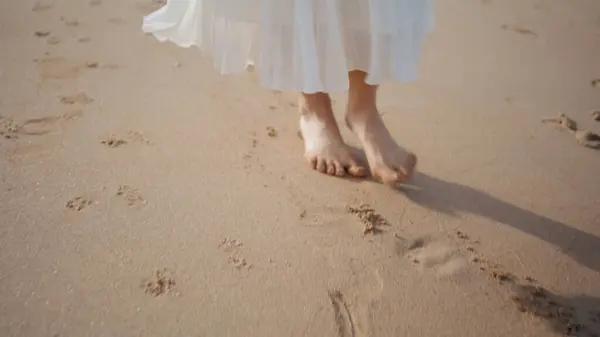 Woman feet stepping sand beach summer day close up. Carefree curly girl walking beautiful ocean shore in white skirt enjoying sunny day. Relaxed model turning around feeling happy on sea coastline.