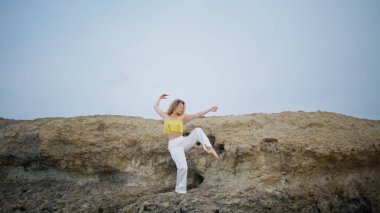 Yumuşak kadın dansçı, esnek vücutla taş gibi bir kayanın üzerinde bacak kaldırıyor. Yetenekli kıvırcık kız yaz doğasında çağdaş dans gösterisi yapıyor. Baştan çıkarıcı genç sanatçı duygusal doğaçlama yapıyor..