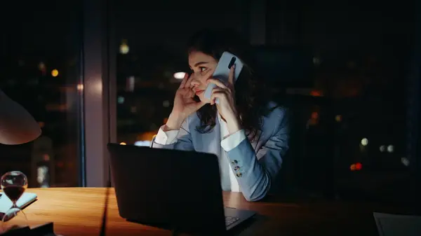 Girl manager complaining at telephone conversation sitting office workplace late evening close up. Tired businesswoman calling phone busy night work. Exhausted woman looking laptop speaking cellphone.