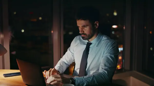 Businessman busy of late work sitting office desk with laptop close up. Overworked bearded corporate manager typing on computer solving business issues at night. Worried employee tired by overtime job