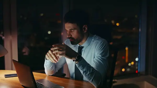 Worried manager sitting at night workplace looking laptop monitor close up. Overwhelmed businessman busy of corporate issues having overtime. Bearded office worker tired of computer work late evening.