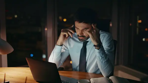 Busy worker speaking telephone at workplace late evening close up. Tired bearded businessman having work phone conversation sitting office desk at night. Overworked sad manager talking at smartphone.
