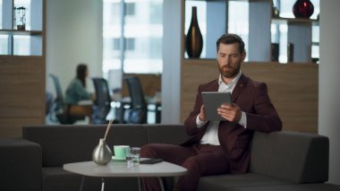 Ofisin iç kısmında yorgun bir yönetici yüzüne dokunuyor. Sakallı profesyonel iş adamı tablet bilgisayarlı büyük bir dolap arıyor. Stresli girişimci modern kurumsal pazarlama işi konsepti.