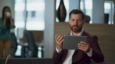 Başarılı bir milyoner ofis içi sanal konferansta konuşuyor. Tablet bilgisayarlı neşeli sakallı iş adamı şirket kabinesini arıyor. Neşeli profesyonel dijital iş mutluluğu kavramı.