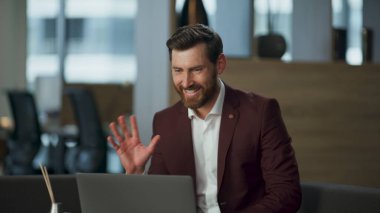 Çekici başarılı yönetmen ofis masasındaki modern dizüstü bilgisayarla görüntülü konuşma yapıyor. Sakallı mutlu yönetici iş arkadaşlarıyla çevrimiçi konferans yaparken gülümsüyor. Konuşan adam görüntülü arama