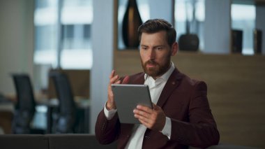 Şirket finans kabinesinde odaklanmış bir avukat tablet bilgisayar ekranı arıyor. Stresli zengin işadamı ofis içi doküman sayfalarını okuyor. Sakallı profesyonel yönetici dijital çalışma konsepti. 