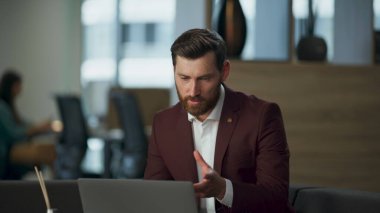 Dost canlısı iş adamı, modern ofiste oturan meslektaşlarıyla görüntülü konuşma yapıyor. Zarif takım elbiseli, kendine güvenen sakallı adam şirket müşterileri online toplantı için laptop web kamerası kullanıyor.