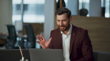 Ofis masasındaki modern laptopla el ele görüntülü konuşma yapan neşeli bir adam. Mutlu yönetici iş arkadaşlarıyla çevrimiçi konferans yaparken gülümsüyor. Başarılı yönetmen konuşma videosu çağrısı