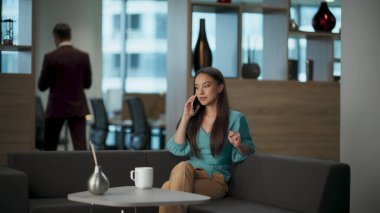 Büyük salonda akıllı telefonla konuşan neşeli bir iş kadını. Mutlu proje yöneticisi dinlenme koltuğu konuşan cep telefonu. Çekici, gevşemiş kadın, ofiste tek başına hücreyi kullanarak konuşmaktan zevk alıyor.