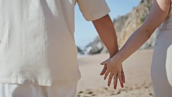 Romantic pair connecting fingers walking tropical ocean coast closeup. Unknown couple enjoying pregnancy spending summer vacation on beach. Pregnant family holding hands relaxing on sandy seashore
