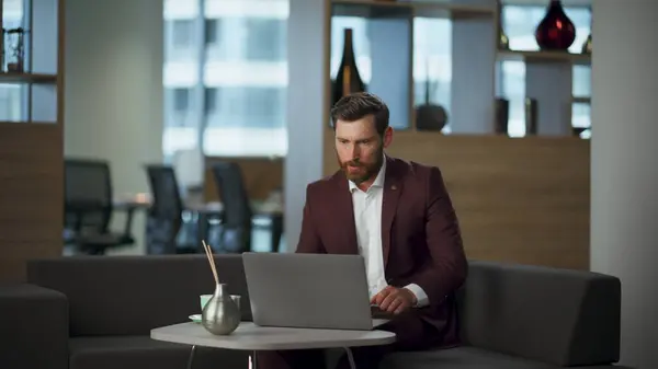 Angry man closed laptop ending annoying work at coworking. Tired businessman disappointed company fail sitting modern workplace. Serious nervous boss feeling sad at hall. Business lifestyle concept