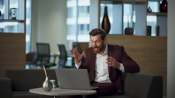 Excited manager gesturing hands looking laptop at office interior. Successful businessman rejoicing success to computer screen winning achievement at corporate room. Happy winner man showing emotions