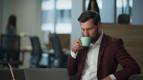Tired professional manager drinking tea in big luxury comfortable cabinet. Stressed wealthy business man looking modern laptop computer screen office interior. Relaxation stressful lawyer work concept