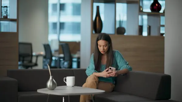 Depressed woman looking cellphone relaxing sofa at coworking space. Pensive upset lady resting couch feeling broken at luxury open space. Sad crying businesswoman holding mobile phone having problems