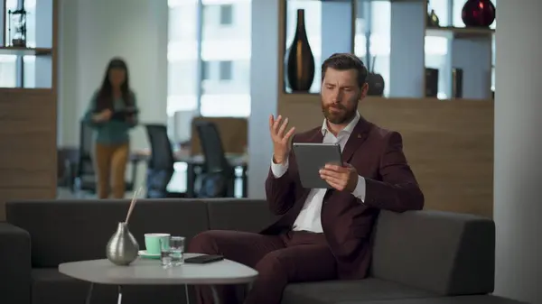 Annoyed entrepreneur working modern tablet computer office interior hall. Tired successful business man touching pad screen big room. Bearded lawyer swiping pages cabinet window. Finance work concept.