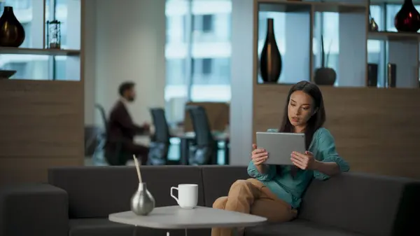 Millennial woman having tablet video conference at office. Busy businesswoman calmly explaining looking tab computer at coworking workplace. Brunette director chatting online using digital device