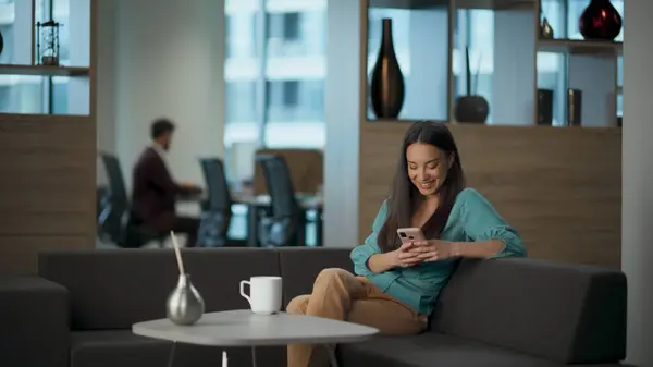 Excited lady laughing smartphone reading jokes at office lounge. Millennial entrepreneur watching funny news online using smartphone. Ceo woman resting at open space workplace. People emotions concept