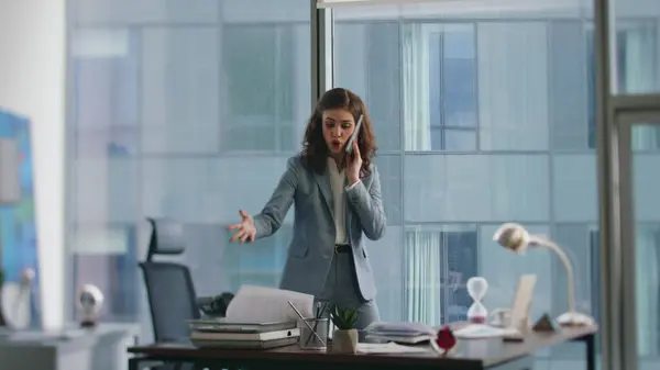 Displeased manager talking telephone emotionally standing at office desk. Annoyed woman ceo complaining at phone conversation worried profit loss. Lady director arguing in smartphone feeling stress.