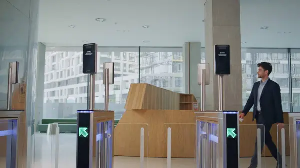 Man entering office automatic gates using electronic card reader at modern building hall. Formal suit worker walking through security turnstile business center. Employee entrepreneur passing entrance.