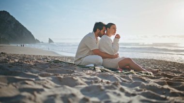 Hamile çift güzel kumsalda piknikte dinleniyor. Rahatlamış genç eşler battaniye oturup yemek yiyorlar ve akşam deniz manzarası harika görünüyor. Sevgi dolu koca, bebek bekleyen kadına sarılıyor..
