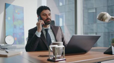 CEO, lüks ofis masasında dizüstü bilgisayarla telefon görüşmesi yapıyor. Başarılı sakallı iş adamı iş yerinde akıllı telefondan konuşuyor. Güvenilir yönetici iş görüşmesi yapan ortakları arıyor.