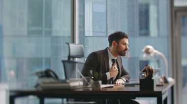 Şirket çalışanı, modern ofis masasında otururken uzaktan konferansa bağırıyor. Duygusal öfkeli iş adamı video görüşmesinde iş sorununu açıklıyor. Sinirli yönetici dizüstü bilgisayarlı web kamerasında gergin bir şekilde konuşuyor.