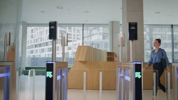 Woman opening automatic gates using smartwatch in modern office building. Confident businesswoman walking through security turnstile business center. Beautiful lady ceo entering in electronic door.
