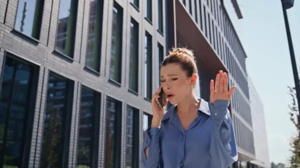 Stressed business woman calling walking urban street sunny morning. Nervous girl manager talking smartphone on go disappointed work problem. Annoyed lady complaining at phone conversation outdoors.