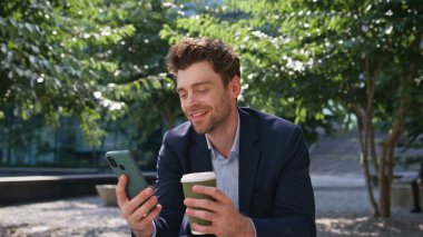 Kahve görünümlü cep telefonu ekranlı Freelancer caddeyi kapatıyor. Gülümseyen yakışıklı iş adamı içecek servisi yapıyor akıllı telefondan mesaj okuyor. Tasasız ofis müdürü tatilin tadını çıkar.