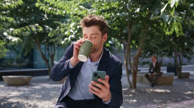 Sunny Park 'ta rahatlamış kahve içen akıllı telefon görünümlü bir çalışan. Cep telefonu tutan gülümseyen yakışıklı adam dışarıda çalışmanın keyfini çıkarıyor. Sunny Caddesi 'nde başarılı bir yönetici cep telefonuna mesaj gönderiyor.