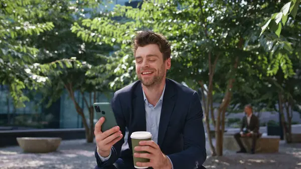 Kahve işadamı Sunny Caddesi 'ndeki akıllı telefondan gülüyor. Happy, cep telefonu park yerinde sosyal medyayı izleyerek rahatladı. Tasasız menajer dışarıda mola vermeyi sever..