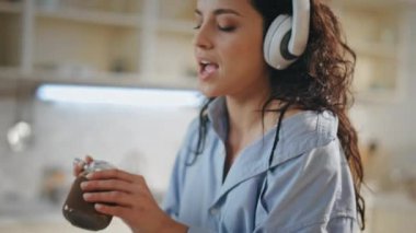Mutfakta modern kablosuz kulaklıkla müzik dinleyen bir kadın. Çekici genç kız bıçaktan çikolata ezmesi tadıyor. Tasasız, rahat ev hanımı kulaklıkla yemek hazırlıyor.