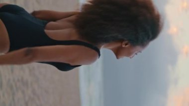 Hayalperest Afrikalı Amerikalı kız kumsalda poz veriyor gür kıvırcık saçlara dikey olarak yakından dokunuyor. Romantik sakin esmer, deniz kıyısında yaz akşamı tek başına duruyor. Siyah mayolu kadın doğanın tadını çıkarıyor.