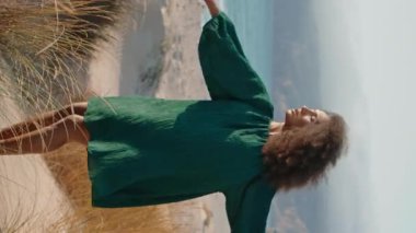 Artistik Afro-Amerikan kadın dansçı. Kum kıyısında dikey olarak kuru otlarla şehvetli dans ediyor. Kıvırcık kız yumuşak eller yapıyor. Esmer, duygusal dans elbisesi içinde