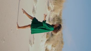 Genç, esnek bir kadın çöl kumullarında dikey siyah elbiseyle modern dans ediyor. Kıvırcık dansçı yaz günü kumsalda gösteri yapıyor. Afro-amerikan güzel kız yumuşak vücut hareketleri yapıyor..