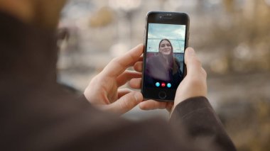 Erkek eller çevrimiçi kız arkadaşını arıyor. Gülümseyen kadın web uygulamasında cep telefonu ekranını sallıyor. Bilinmeyen erkek arkadaş sokakta akıllı telefonlu uzak bir kızla konuşuyor. Video konferansı kullanan mutlu çift