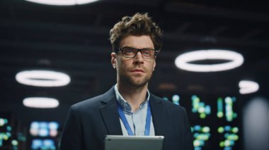 Yazılım geliştiricisi sunucu odasında poz veriyor. Gözlüklü yakışıklı bir iş adamı. Uzakta veri merkezinde çalışıyor. Bilgisayarlar rafta zum yapıyor. Yetkili mühendis tek başına iş yerinde duruyor.