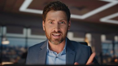 Pozitif patron akşam odasında duygusal olarak el hareketleriyle konuşuyor. Gülümseyen iş adamı video konferansı yapıyor. İyi girişimciler gece ofisinde online toplantı yapıyor. Modern teknoloji