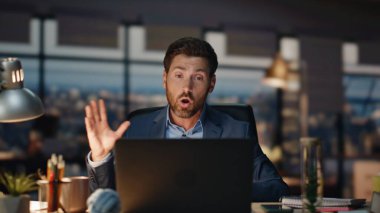Sinirli adam akşam iç mekanda video görüşmesini tartışıyor. Duygusal olarak rahatsız olan yönetmen bilgisayardaki görüntülü sohbette el kol hareketi yapıyor. Sinirli iş adamı geceleri bilgisayarın sesini yükseltiyor.