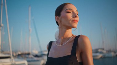 Huzurlu gezgin rıhtımda dinleniyor ve yumuşak akşam güneşinin tadını çıkarıyor. Bronz tenli kadın lüks yatların önünde okyanus rıhtımında dikiliyor. Güzel güneşli limanda poz veren çekici kız modeli.