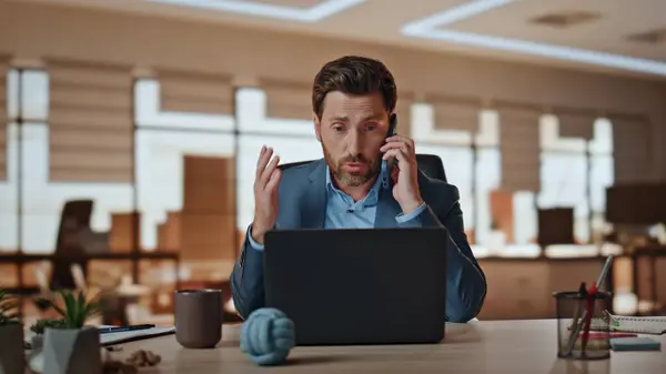 Man banker calling client having nervous conversation in office closeup. Dissatisfied ceo arguing mobile phone sitting workplace. Furious businessman gesturing hands scolding subordinator at call