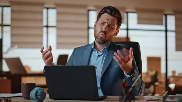 Disappointed man reacting fail at private cabinet workplace. Mad loser feeling displeased working at modern office. Upset businessman gesturing hands hitting laptop table emotionally. Work problems