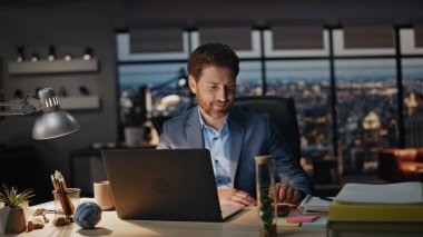 Gece dolabında cep telefonu ekranına bakan mutlu bir adam. Gülümseyen patron panoramik karanlık ofiste akıllı telefon okuyordu. Akıllı yönetmen cep telefonunu bilgisayar işyerinde açıyor